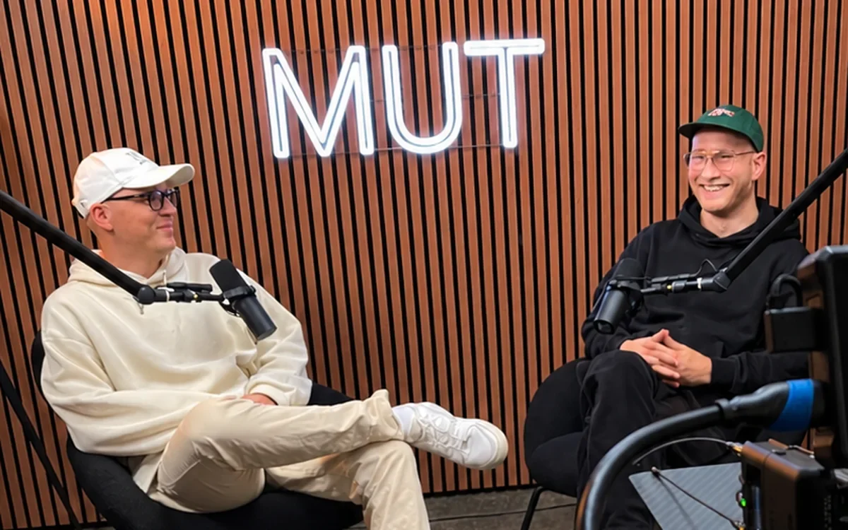 Zwei Podiv-Macher bei einer Aufnahme im Podcast-Studio vor dem Neonschriftzug MUT